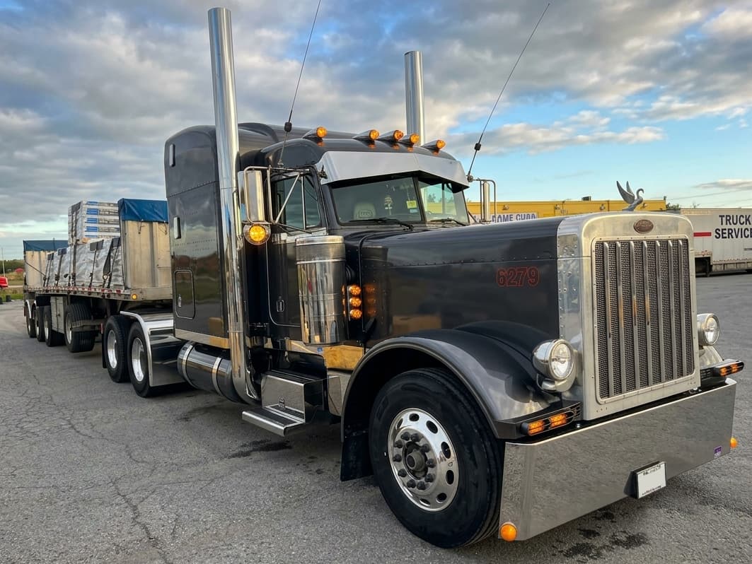 A black Peterbilt tractor hitched to a loaded flatbed trailer